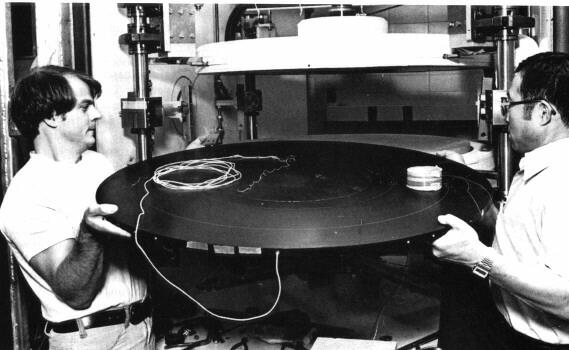 Two men with a large circular object. black & white