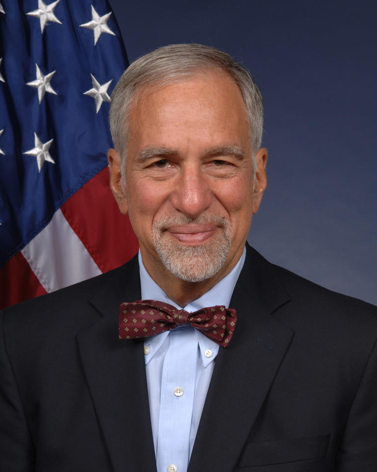 Headshot of Phillip Singerman in a bowtie. American flag in background