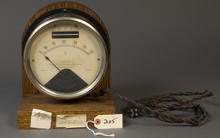 A wood-framed round dial face with numbers running from 0 to 35, with the 25 gradation marked in red.  