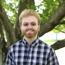 portrait of Paul Neves, a blond man with a dark beard and glasses