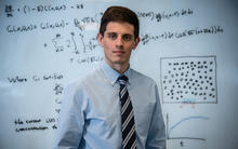 Mathematician Ryan Evans in front of a whiteboard covered in mathematical equations