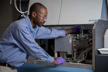 Chemist Savelas Rabb is bent over slightly, using a tool to check on the settings inside of a large instrument known as a mass spectrometer.