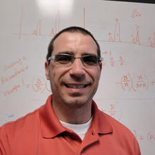 portrait of Adam Pintar in front of a whiteboard covered with equations