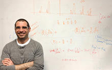 Adam Pintar standing with arms crossed in front of a whiteboard covered with equations and graphs