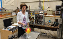 Woman standing in a lab holds a rectangular radiation detector near a metal globe that has been painted with a radiation symbol