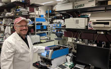 smiling man with a red baseball cap and white lab coat on in a laboratory full of instruments