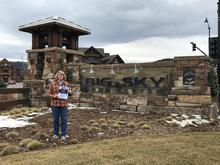 Pat Lapekas stands outside in front of big rocks with Baldrige booklet in hand