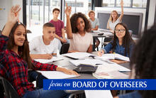Focus on Overseers Pat Greco image of students raising their hands to answer teacher's question.