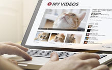 YouTube like interface on a laptop screen. The text on the screen reads "my videos" and there are several tiles displaying various cat videos below.