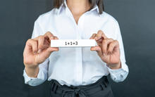 Hybrid female employee holding a card that says 1+1=3.