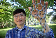 Ming Zheng stands outside smiling and holding a model of a nanotube made of a lattice of smaller tubes.