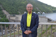 Jeffrey Fong poses smiling in front of a railing overlooking a concrete dam. 