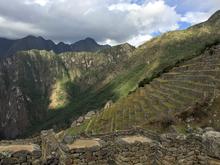 Sun and shade play over green and rocky mountains and terraces outlined with stone walls. 