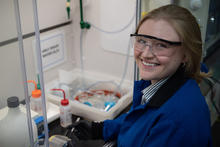 Christine McGinn wears safety glasses as she handles plastic bottles and other materials in the lab. 