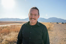 Zach Grey poses outdoors with wind turbines in the background. 