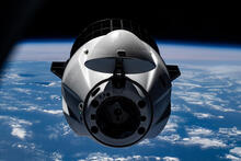 A rounded spacecraft floats in space with the blue surface of the Earth in the background.