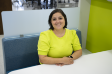NIST researcher Carina Hahn, wearing a lime green sweater, sits at a white table and smiles at the camera. 