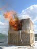 Flames coming out of the first doorway of a test structure after the floor has collapsed into the basement.