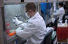 Man in white lab coat using a pipette under a hood