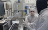 Man and woman in lab gear in front of computer screen in clean room