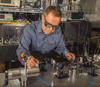 Man in striped shirt wearing laser safety glasses working with laser table in laboratory.