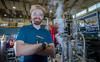 Young man with wild blonde hair and reddish beard smiling beside an AC susceptometer that he helped build