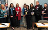 A group of men and women stand facing forward with nametags within an office building room.