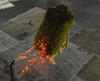 A rectangular-shaped model of a thatched roof is attacked by embers emitted from the pipe-shaped mouth of the NIST Dragon device.