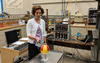 Woman standing in a lab holds a rectangular radiation detector near a metal globe that has been painted with a radiation symbol