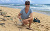 woman kneeling on a Hawaiian beach putting plastic trash into a bag