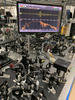 Table covered with lenses and other optical equipment, and a flat screen mounted high in the background showing a yellow squiggly line across the top and a spiky orange line below.