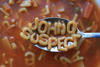 A spoon hovers above a bowl of alphabet soup. On the spoon are the letters JOHN Q SUSPECT. 