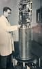 A man in a lab coat stands to the left of a tall piece of equipment