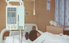 Infusion pump in foreground of hospital room with patient lying in bed