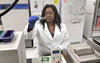 young woman in a lab coat looks at vials with a small amount of green liquid in them before putting them into a machine