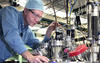 man with goggles, blue shirt and blue cap adjusts a pipe on top of a gleaming aluminum ultra-high vacuum (UHV) metal deposition chamber