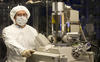 Andras Vladar in a white gown, hairnet and mask with a scanning electron microscope.