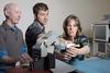 Two men and a woman stand at a table holding a robotic arm. 