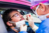 A medical worker administers a nasal swab test to a person in a car. 
