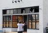 A man faces away from the camera, taking a photo of a damaged storefront.