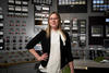 A woman stands in front of a wall full of knobs and switches.