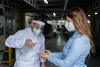 Man at the door of factory applying alcohol to the hands of the workers arriving to work