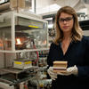 A woman wearing safety goggles (Laura Dubrulle) hold a stack of square wood samples in a scientific lab. 