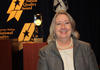Photo of Barbara Fischer standing in front the the Baldrige Award Crystal.
