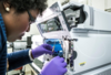 A woman wearing purple gloves adjusts tubing inside a scientific device.