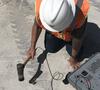 Person in hard hat is tapping concrete with a hammerlike device.