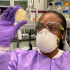A scientist wearing protective gear holds up a petri dish.