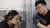 Two researchers examine a cylindrical metal device used to trap ions.