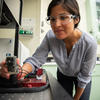 Polette Centellas wears safety glasses as she leans toward the camera while adjusting a scientific device on a lab table. 
