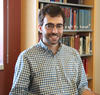 Adam Kaufman poses for a head shot with a shelf of library books in the background. 